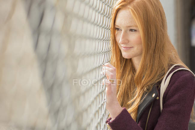 Mujer mirando a través de la cerca de eslabones de cadena - foto de stock