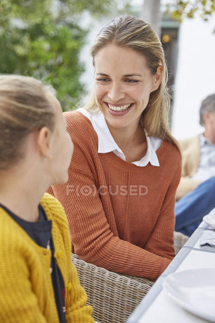 Усміхнена мати і дочка розмовляють за столом патіо — стокове фото