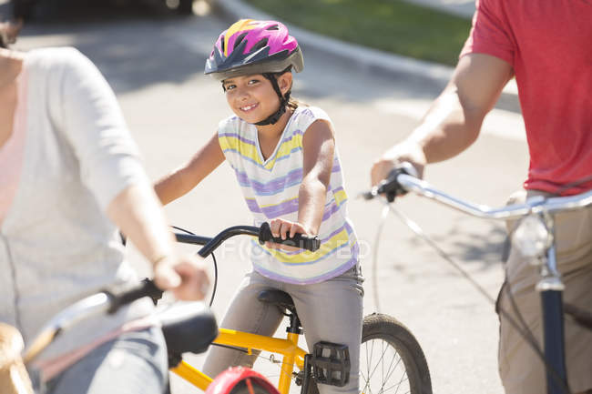 Retrato de niña sonriente montando en bicicleta con los padres - foto de stock