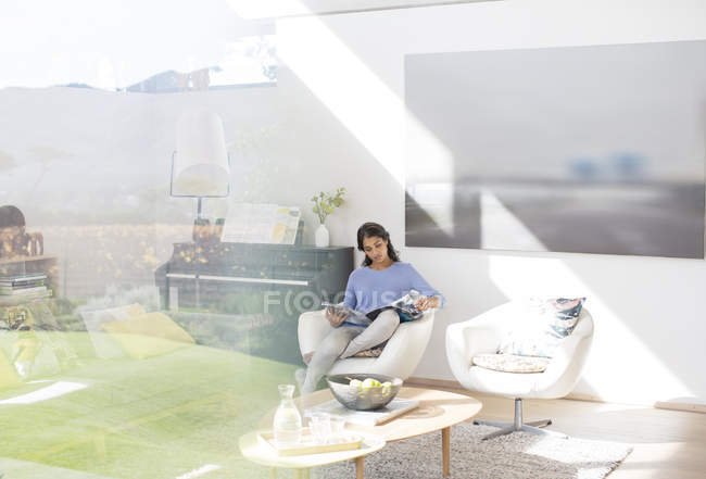 Donna che legge rivista in soggiorno soleggiato — Foto stock