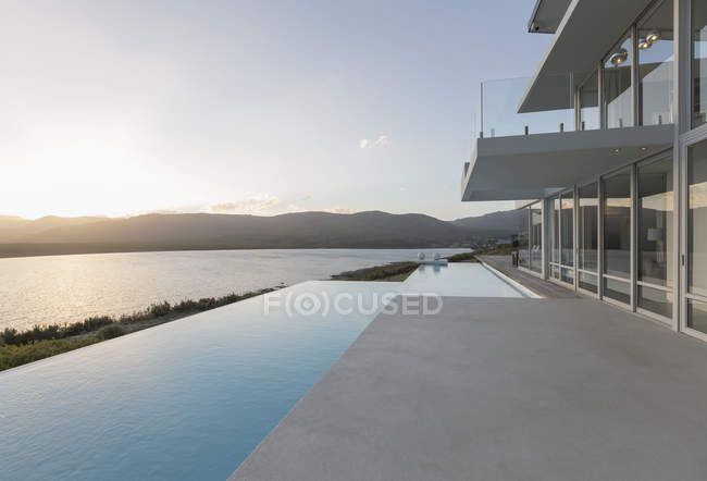 Sunny, tranquilo casa de luxo moderno vitrine exterior com piscina infinita e vista para o mar por do sol — Fotografia de Stock