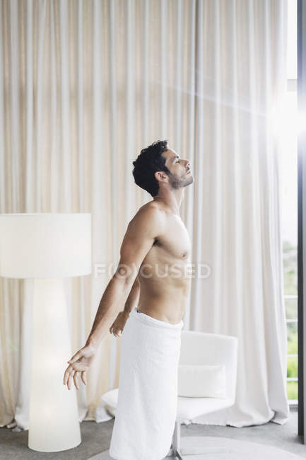 Человек в полотенце купается в солнечном свете у окна спальни — стоковое фото