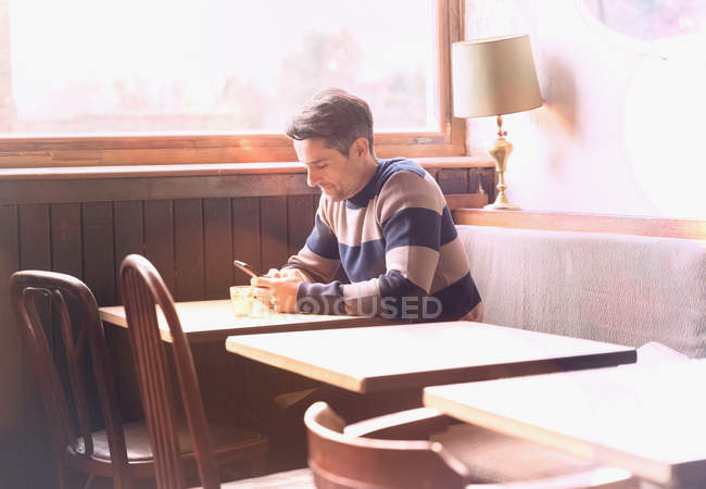 Людина текстові повідомлення з мобільного телефону за столом в Сонячний кафе вікно — стокове фото