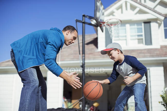 Padre e hijo jugando baloncesto en la soleada entrada - foto de stock