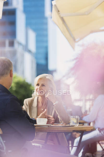 Imprenditrice che ascolta un uomo d'affari al soleggiato caffè sul marciapiede urbano — Foto stock
