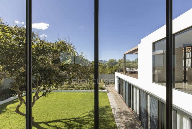 Vista de janelas de casa de luxo moderno ensolarado vitrine exterior com quintal e árvore — Fotografia de Stock