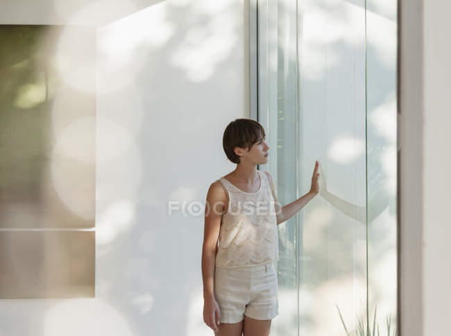 Mulher pensativa em pé na janela ensolarada — Fotografia de Stock
