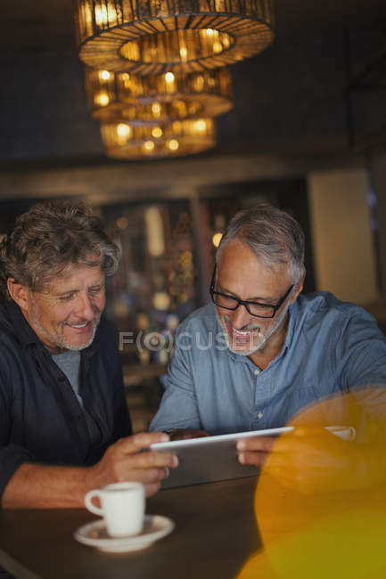 Мужчины, использующие цифровой планшет и пьющие кофе за столом ресторана — стоковое фото
