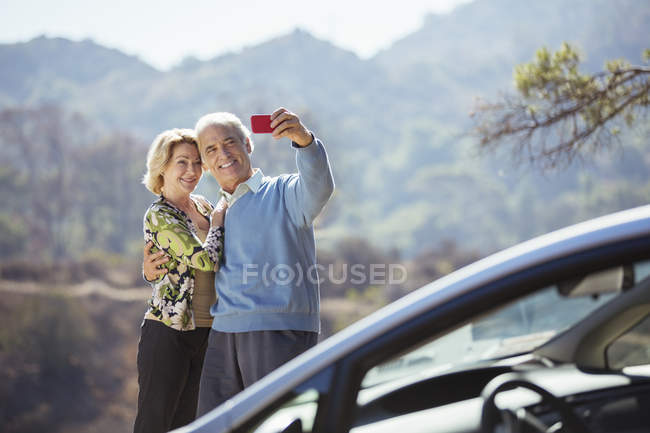 Couple âgé prenant autoportrait avec téléphone portable à l'extérieur de la voiture — Photo de stock