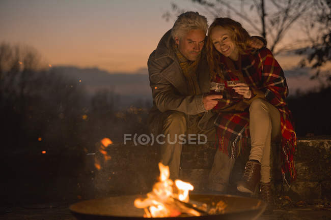 Couple drinking enjoying autumn campfire — Stock Photo