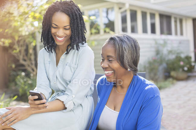 Smiling mother and daughter text messaging with cell phone on patio — Stock Photo