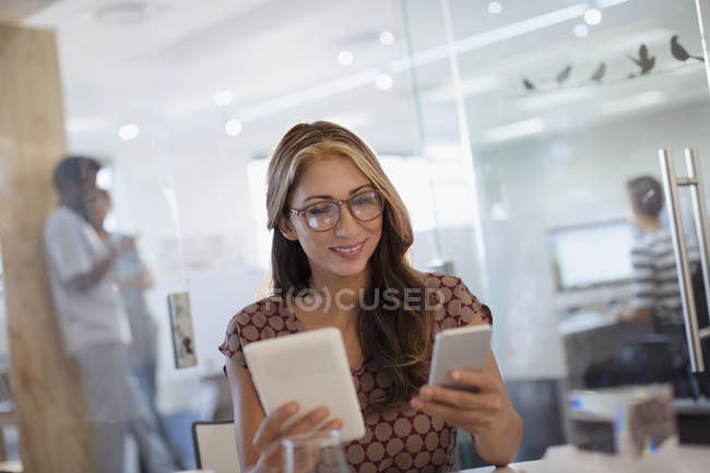 Empresária multitarefa, usando telefone inteligente e tablet digital no escritório — Fotografia de Stock