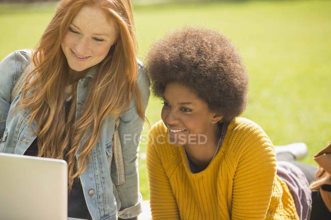 Mujeres jóvenes felices usando el ordenador portátil en el parque - foto de stock