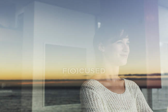 Donna con vista tramonto e oceano dalla finestra — Foto stock