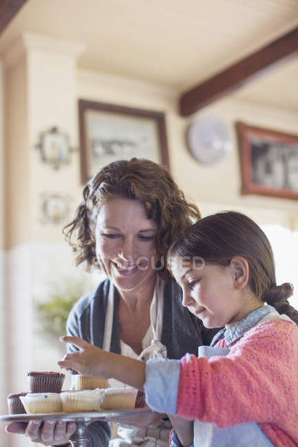 Abuela y nieta colocando cupcakes en la bandeja - foto de stock