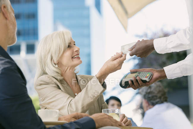Serveur payant femme d'affaires avec lecteur de carte de crédit au café trottoir urbain — Photo de stock