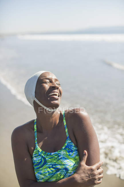 Mujer en traje de baño y gorra riendo en la playa - foto de stock