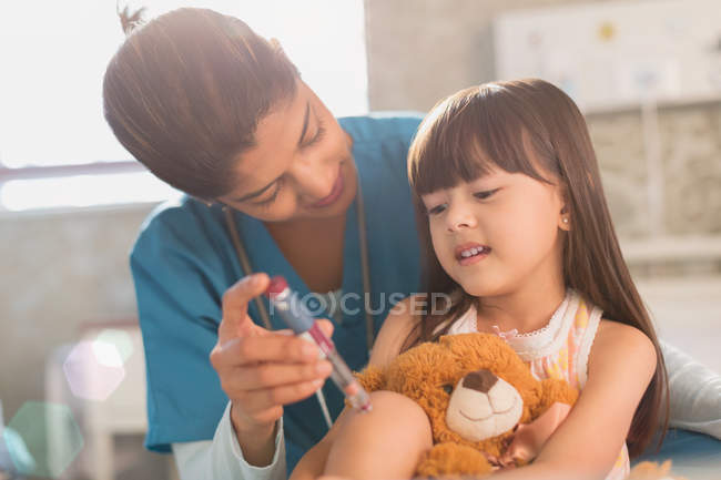 Enfermera mujer enseñando paciente niña con osito de peluche cómo usar pluma de insulina - foto de stock