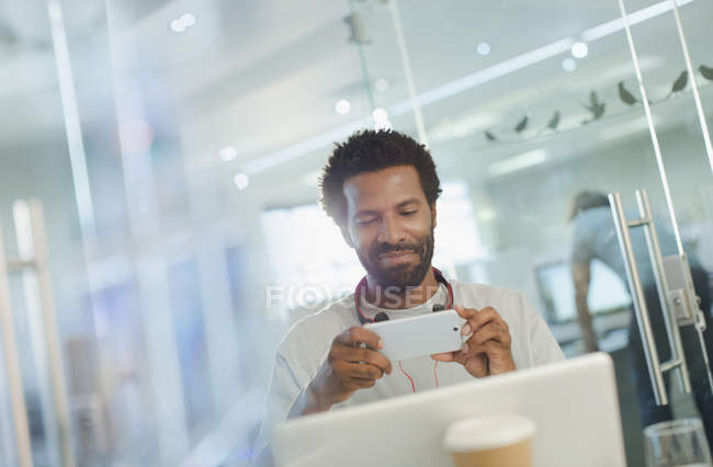 Empresário criativo sorrindo usando telefone inteligente no laptop — Fotografia de Stock