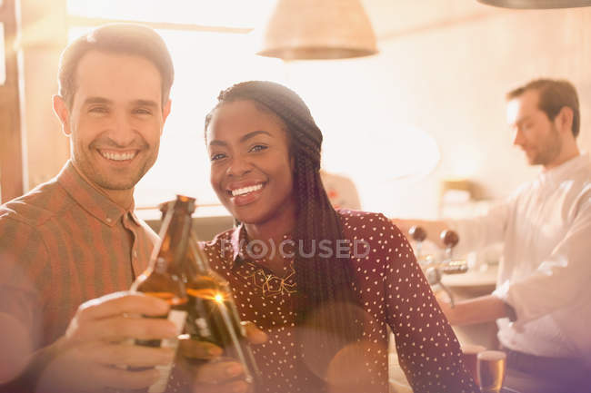 Ritratto coppia sorridente brindare bottiglie di birra nel bar — Foto stock