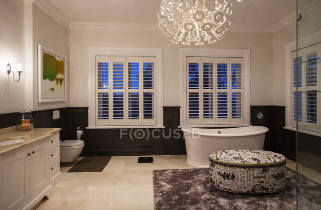 Soaking tub and modern chandelier in luxury bathroom at night — Stock Photo