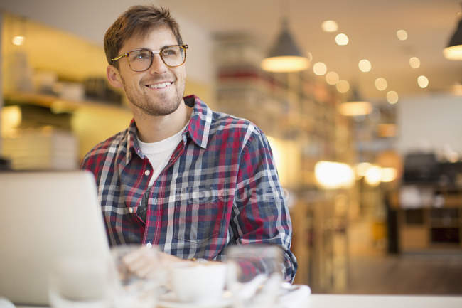Happy young man using laptop in cafe — Stock Photo