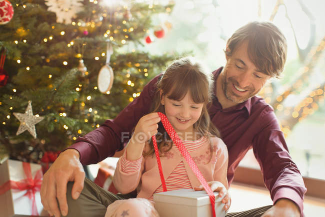 Батько спостерігає за дочкою, яка відкриває різдвяний подарунок — стокове фото