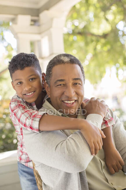 Primer plano retrato de sonriente abuelo y nieto abrazando en porche - foto de stock