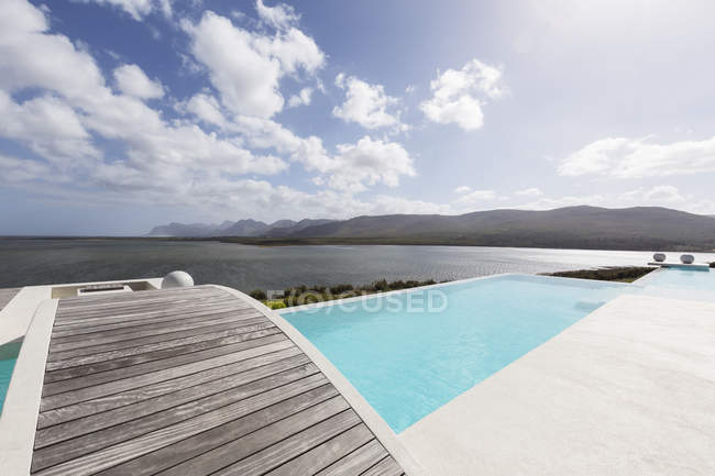 Piscine à débordement de luxe moderne ensoleillée avec passerelle et vue sur l'océan — Photo de stock