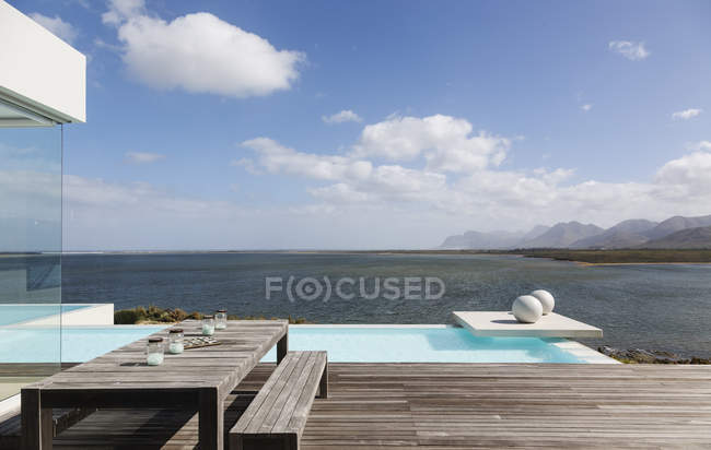 Pátio de luxo moderno tranquilo ensolarado com piscina infinita e vista para o mar — Fotografia de Stock