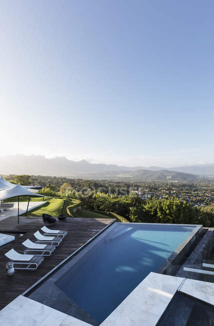 Home showcase exterior infinity pool and patio with mountain view under sunny blue sky — Stock Photo