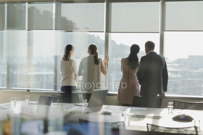 Les gens d'affaires regardent par la fenêtre ensoleillée dans la salle de conférence urbaine — Photo de stock