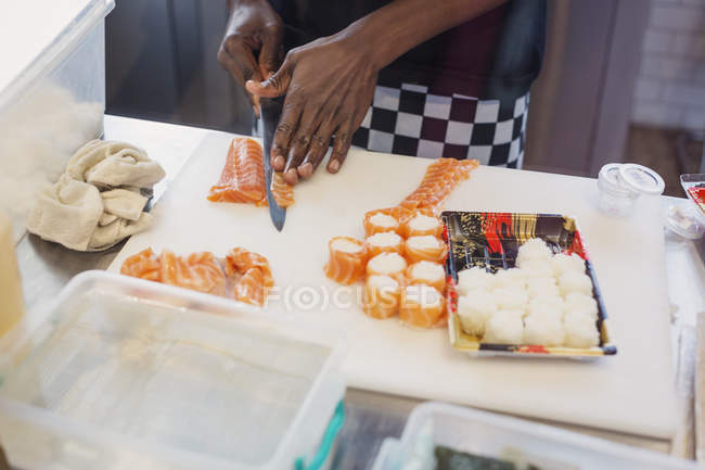 Young female chef slicing salmon, making sushi in restaurant — Stock Photo