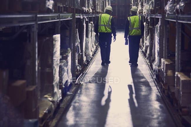 Vista trasera de los trabajadores que caminan en el pasillo de almacén de distribución - foto de stock
