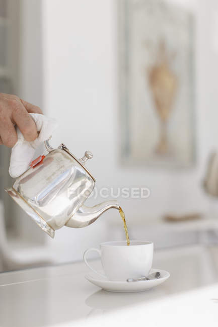 Hand gießt Tee aus silberner Teekanne — Stockfoto