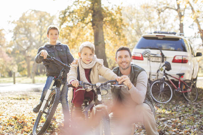 Retrato padre e hijos con bicicletas en el parque de otoño - foto de stock