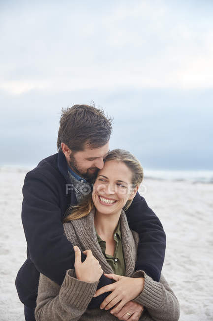 Liebevoll lächelndes Paar umarmt sich am Winterstrand — Stockfoto