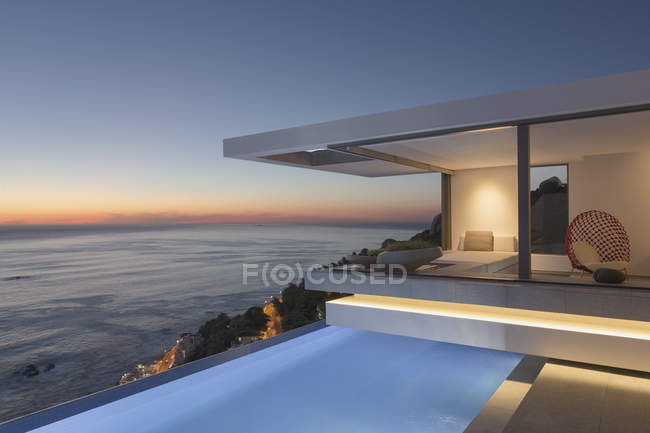 Illuminated modern, luxury home showcase exterior patio with lap pool and ocean view at twilight — Stock Photo