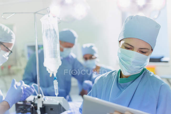 Жіночий хірург носіння хірургічну маску, використовуючи цифровий планшетний в операційний зал — стокове фото