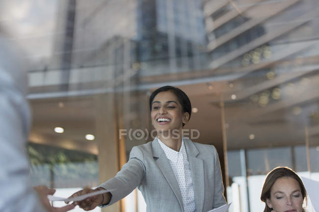 Усміхнена бізнес-леді передає документи колезі на засіданні конференц-залу — стокове фото