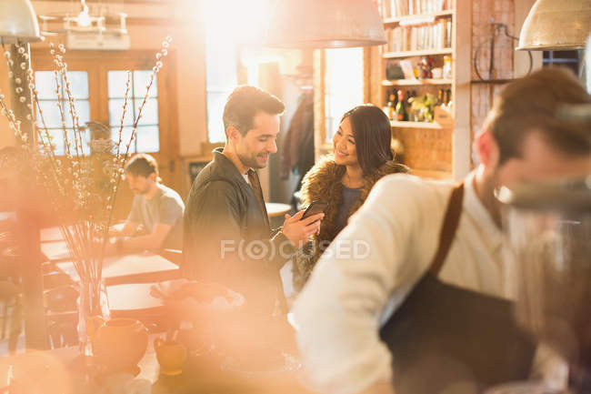 Feliz pareja usando el teléfono celular en la cafetería - foto de stock