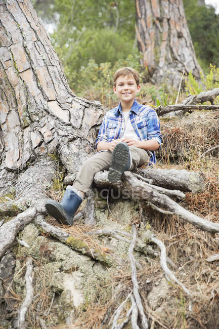 Niño sentado en las raíces del árbol en el bosque - foto de stock