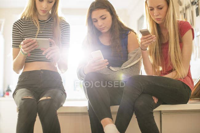 Teenager-Mädchen, die mit Mobiltelefonen in der Küche SMS schreiben — Stockfoto