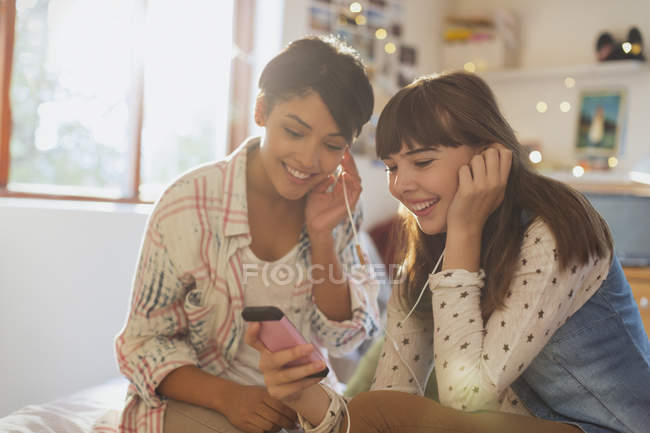 Молоді жінки друзі діляться навушниками, слухаючи музику з mp3 плеєром — стокове фото