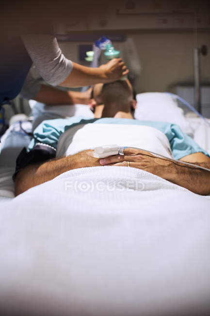 Enfermeira feminina segurando máscara de oxigênio sobre a boca do paciente masculino em unidade de terapia intensiva — Fotografia de Stock