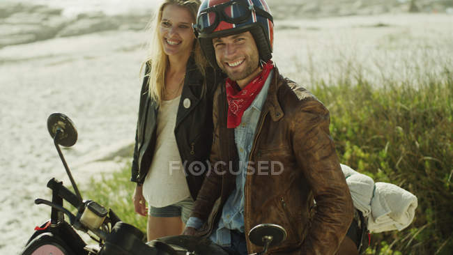 Portrait smiling young couple at motorcycle on beach — Stock Photo