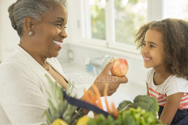 Grand-mère heureuse donnant la pomme à petite-fille dans cuisine — Photo de stock