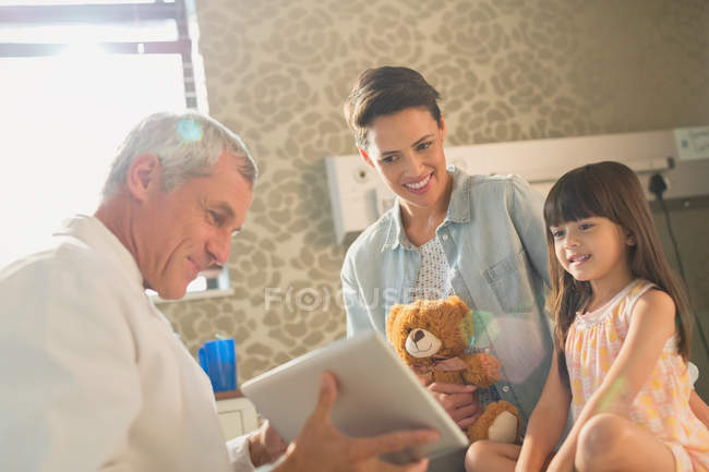 Male doctor showing digital tablet to girl patient and mother in hospital room — Stock Photo