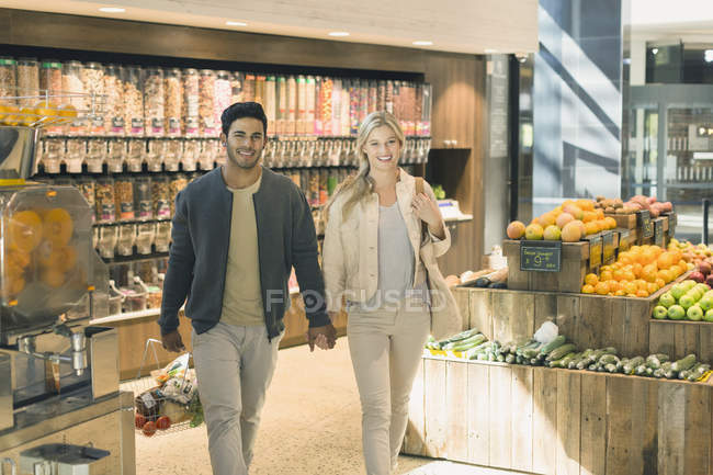 Retrato joven pareja cogida de la mano, compras de comestibles en el mercado - foto de stock