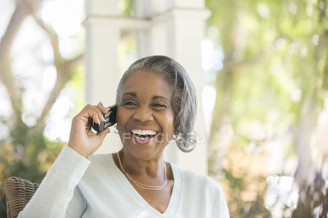 Энтузиастичная пожилая женщина разговаривает по телефону на крыльце — стоковое фото